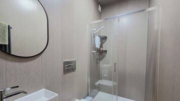 Un baño moderno con lavamanos, espejo y ducha con mampara de vidrio.