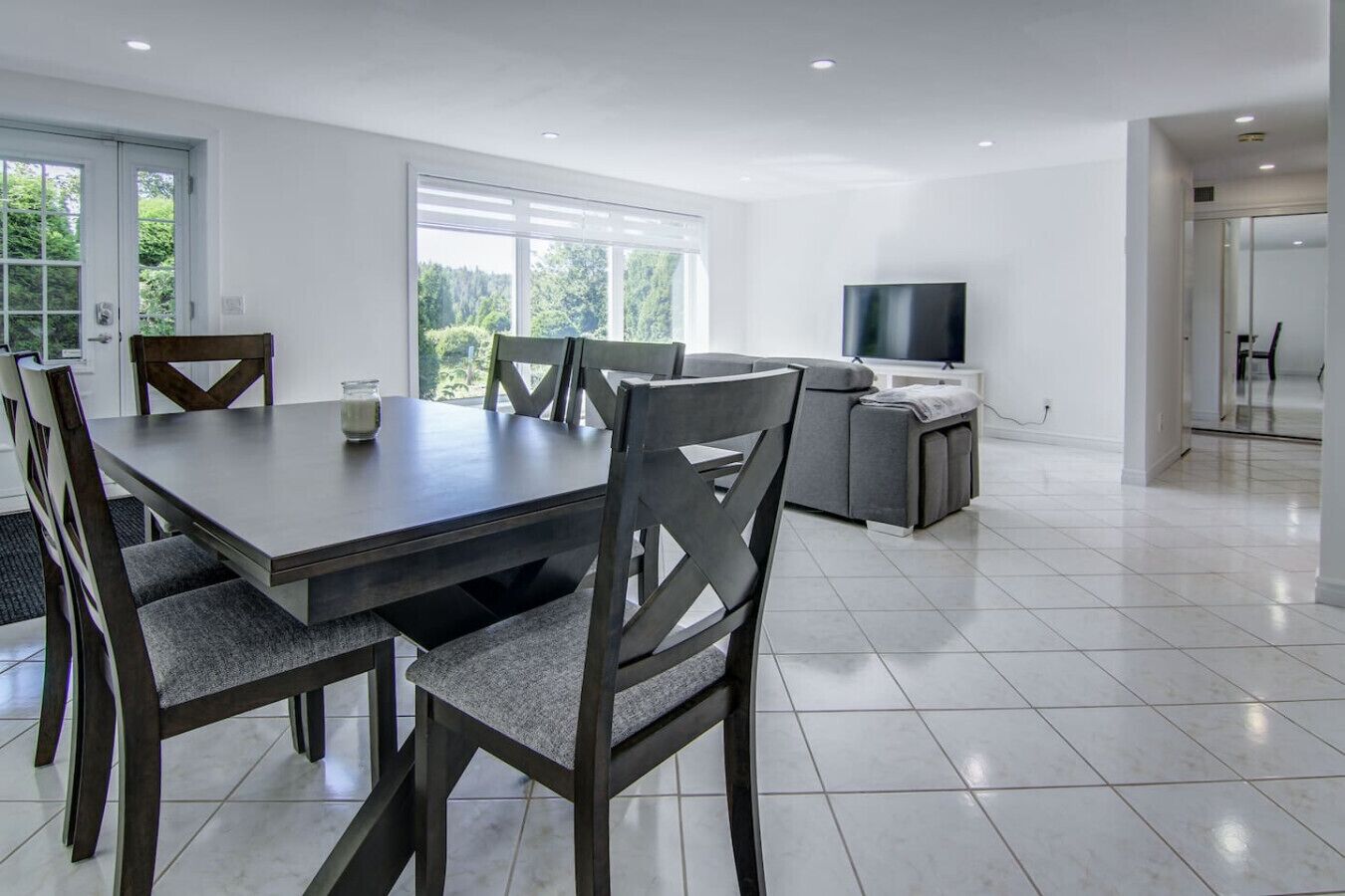 A modern kitchen with a dining area, large windows, and a flat-screen TV.