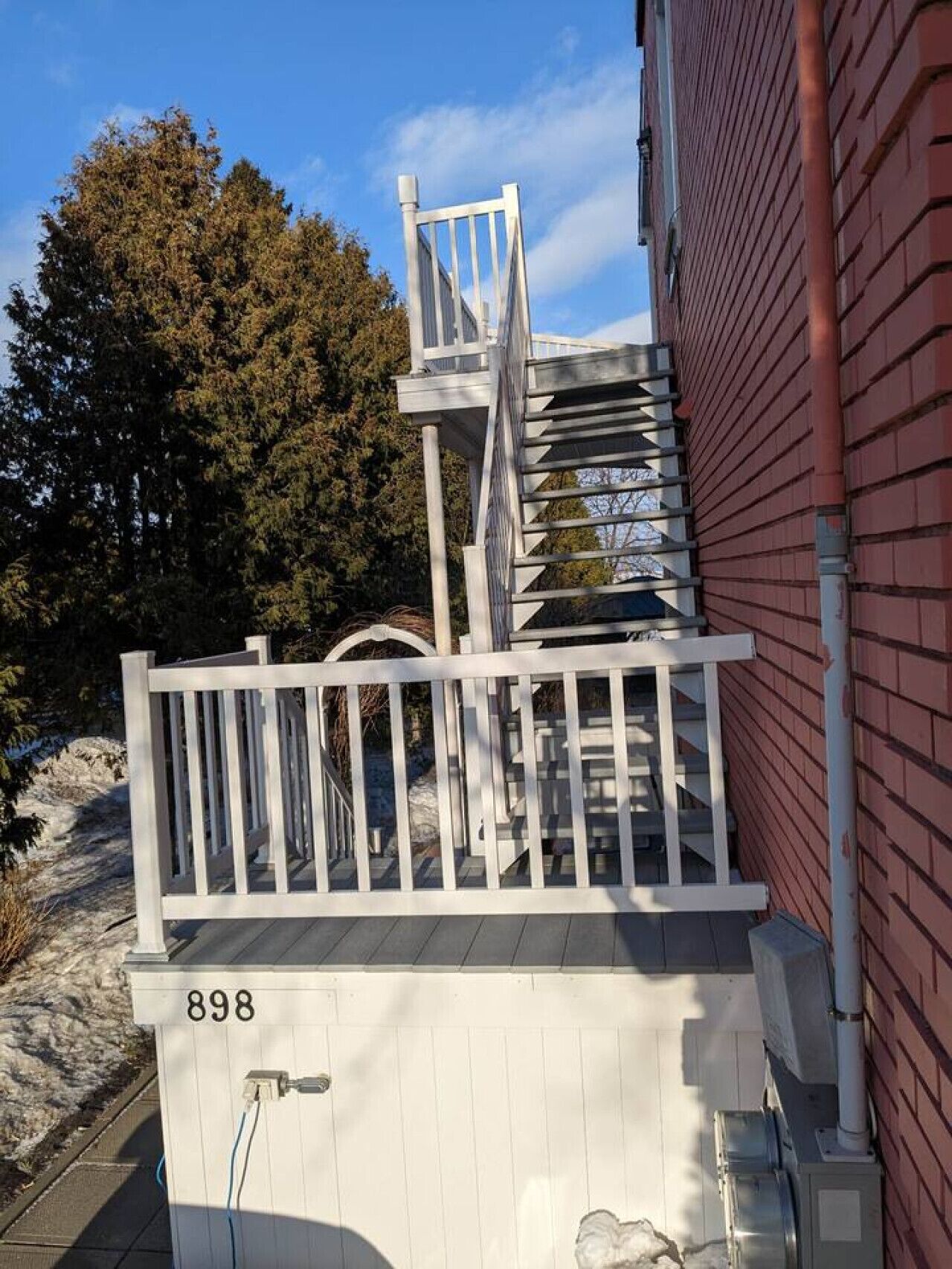 Eine weiße Holztreppe mit Geländer, die zu einem Gebäude aus roten Ziegeln führt.
