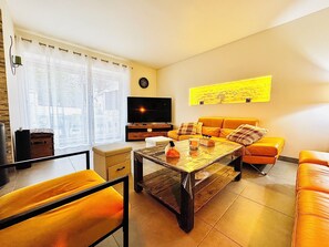 Una sala de estar con un sofá, una mesa de centro, un televisor y una ventana con cortinas.