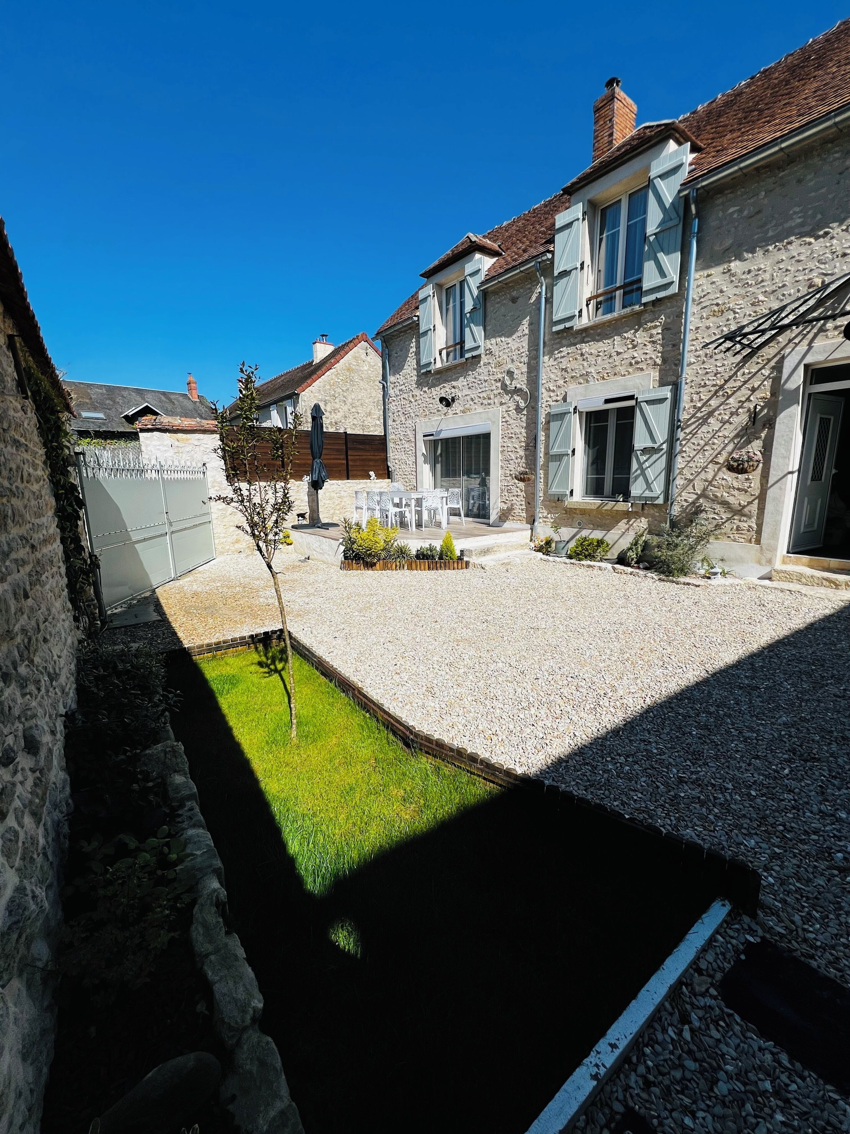 Une maison en pierre avec une allée en gravier, une petite pelouse et un espace patio.