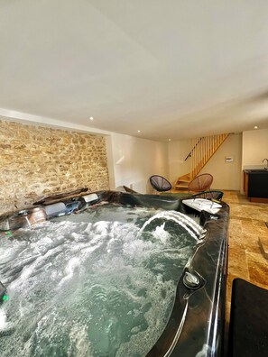 Tinaja de hidromasaje en una habitación con paredes de piedra, una escalera y muebles modernos.
