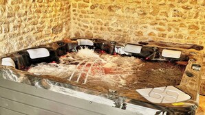 Uma banheira de hidromassagem com um painel de parede de pedra, um banco e piso ladrilhado.