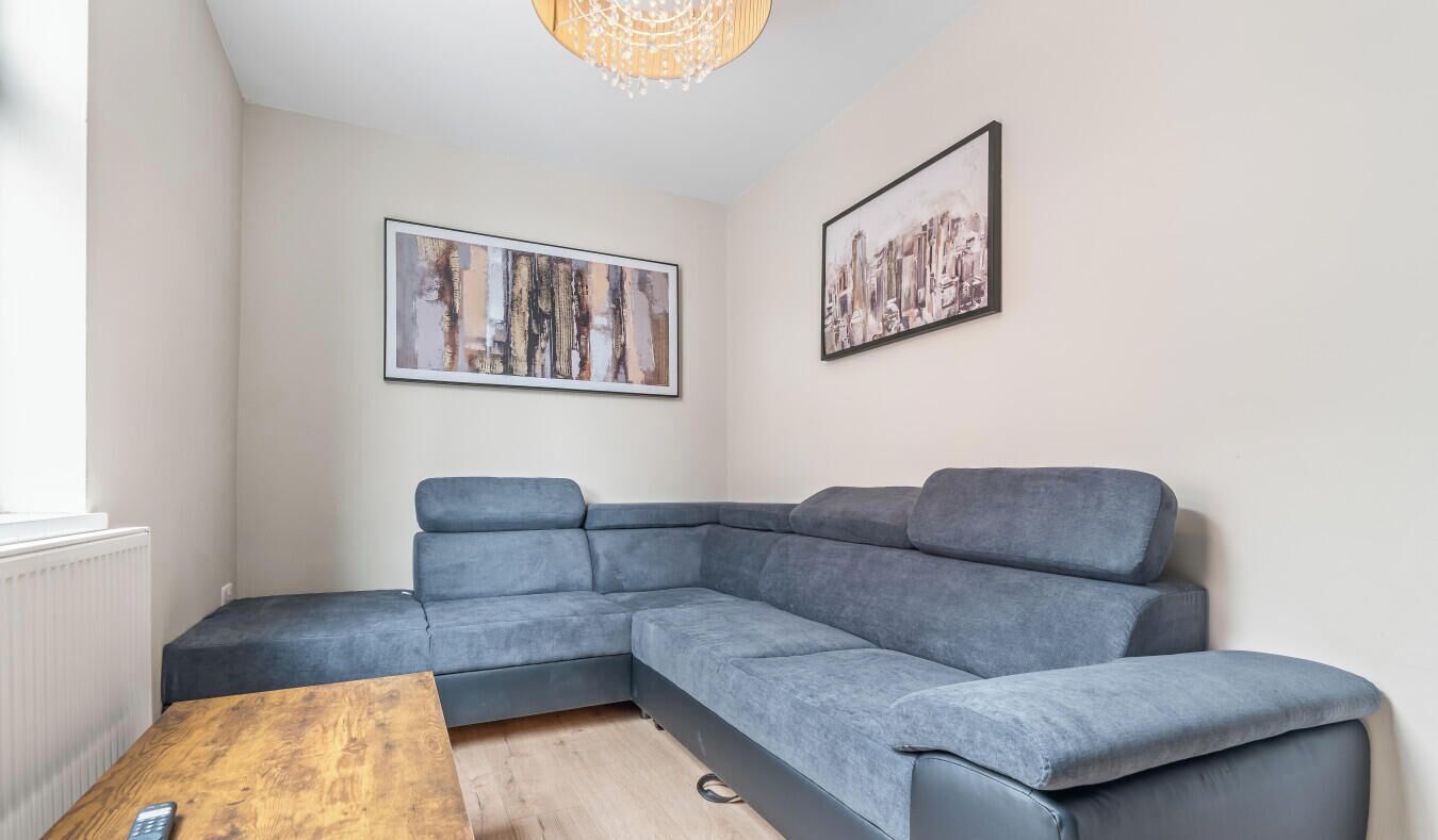 Un salon moderne avec un canapé d’angle gris, une table basse en bois et deux œuvres d’art encadrées accrochées au mur.