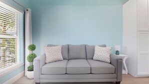 A grey sofa with patterned pillows, a small potted plant, and a white side table with a lamp. - New! Charming Lilac Cottage 111 (Punta Gorda)