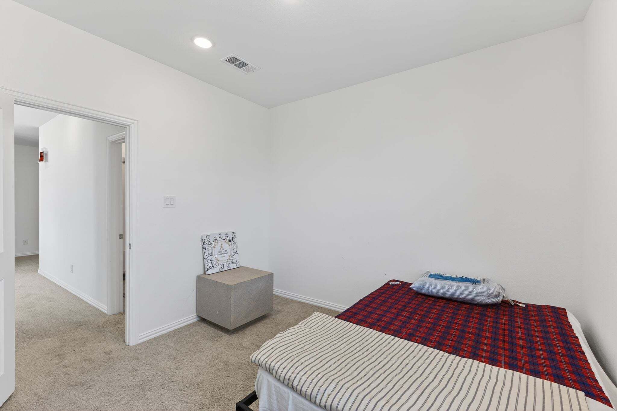 A bedroom with a bed, a small stool, and a door leading to another room.