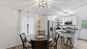 Een moderne keuken met witte kasten, een centraal eiland, barkrukken en een eettafel met stoelen.