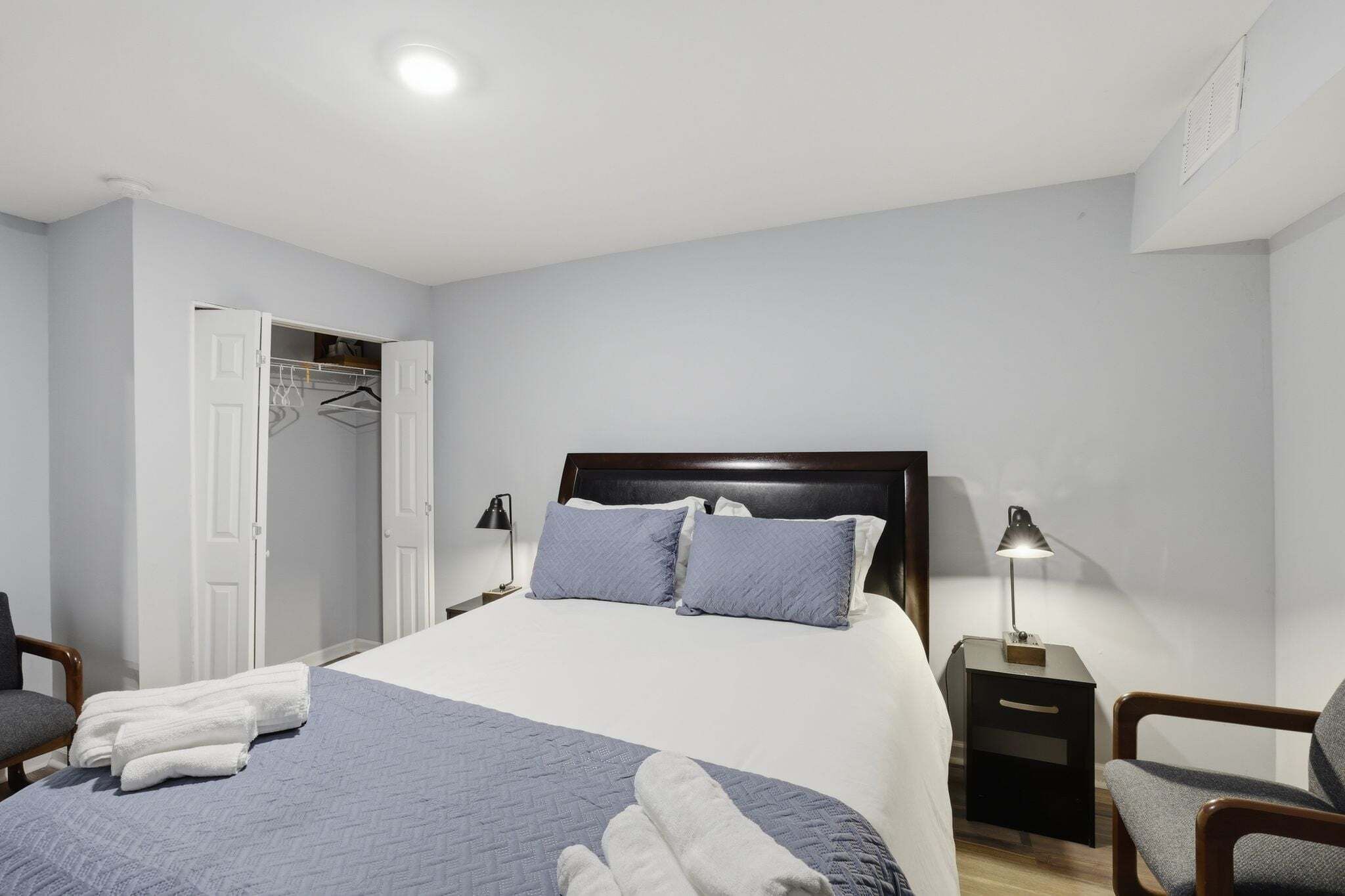 A neatly arranged bedroom with a bed, bedside tables, a chair, a wardrobe, and a nightstand.