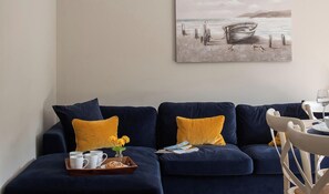 Un salon avec un canapé bleu foncé, des coussins jaunes, un plateau sur lequel se trouvent une cafetière, des tasses et des fleurs.