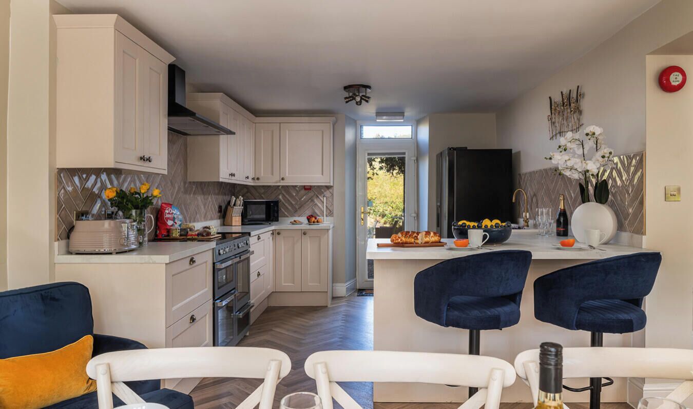 Une cuisine moderne avec des meubles blancs, un réfrigérateur noir et un coin repas avec des chaises bleues.