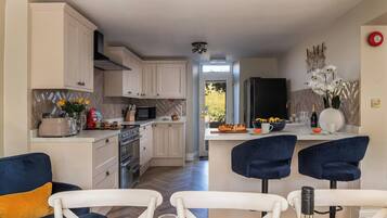 Une cuisine moderne avec des meubles blancs, un réfrigérateur noir et un coin repas avec des chaises bleues.
