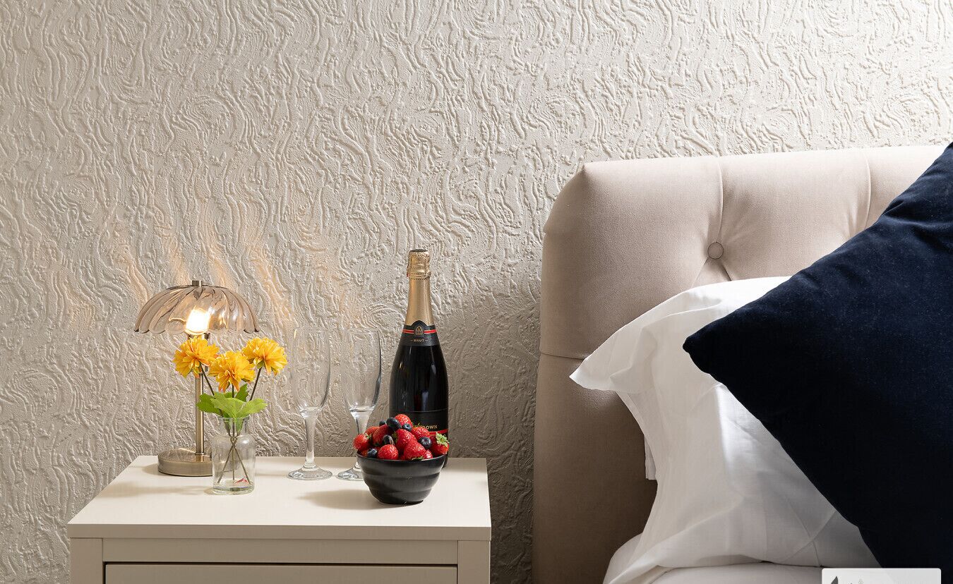 Ein Nachttisch mit einer Weinflasche, einer Obstschale und einer Lampe.