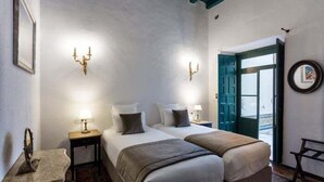 Une chambre d’hôtel avec deux lits, une petite table, une chaise, un miroir et une porte donnant sur l’extérieur.