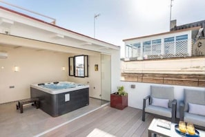 Ein moderner Außenbereich mit Whirlpool, umgeben von Glas, einem Holzdeck und einer Sitzgruppe mit Tisch und Stühlen.