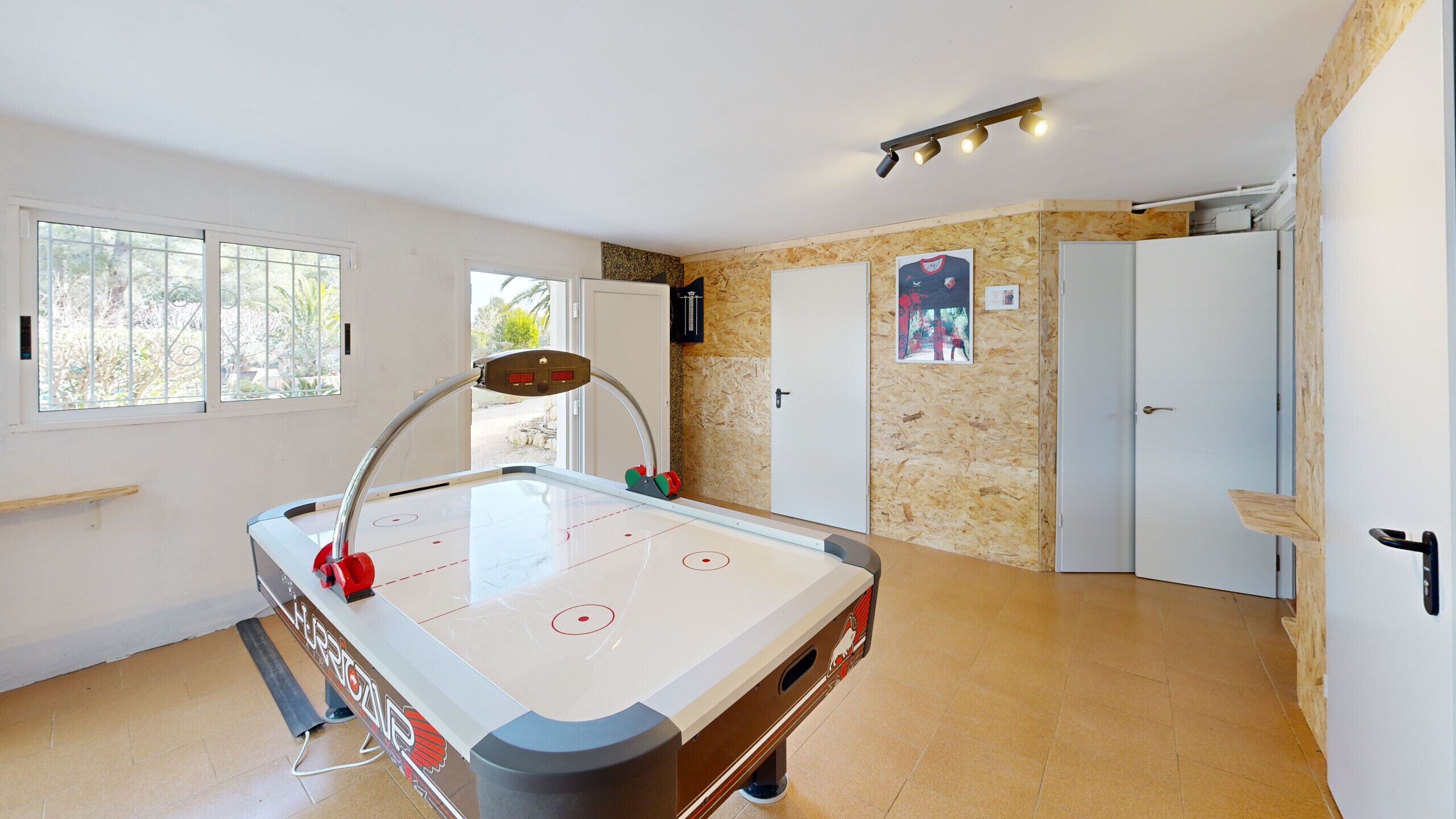 A pool table with a cue stick, a door, and a window with a view of trees.
