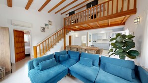 Uma sala de estar moderna com um sofá de canto azul, uma escada de madeira e uma cozinha ao fundo.