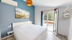 Quarto com cama, pintura, luminária no teto e vista através de uma porta de vidro.
