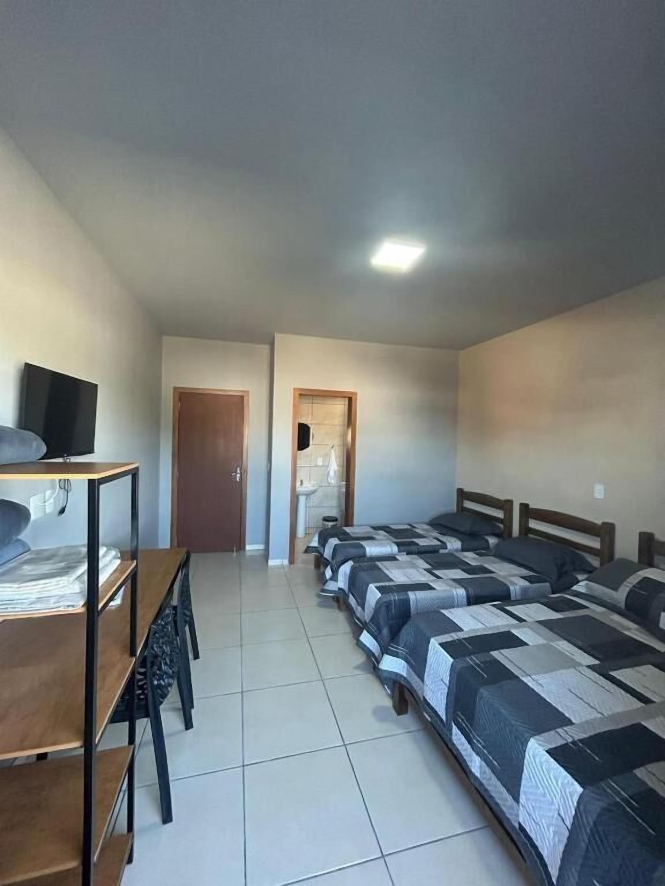 Una camera d'albergo con un letto, una scrivania, una sedia, una televisione e l'ingresso del bagno.
