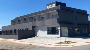 En modern byggnad med ett platt tak, flera fönster och en skylt med texten ”POUSADA”.