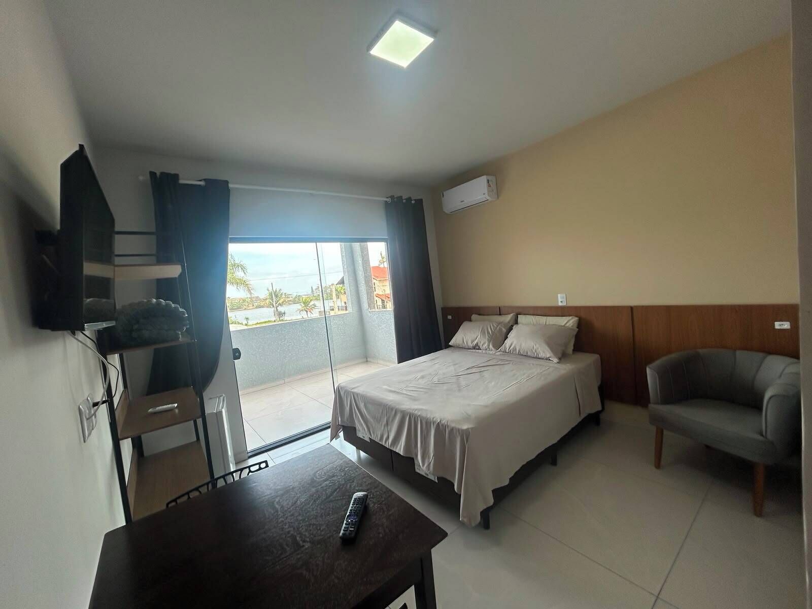 Habitación de hotel con cama, una silla, una mesa, televisión y balcón con vistas.