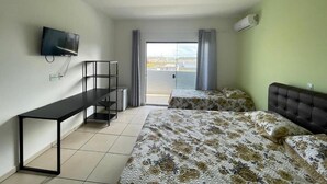 Ett hotellrum med en säng, ett skrivbord, en TV och en balkong med gardiner.