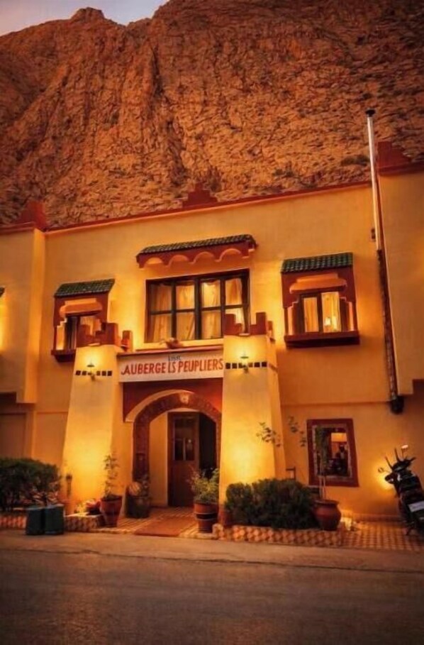 A building with a sign reading 'AUBERGE LES PEUPLIERS' and a mountain backdrop.