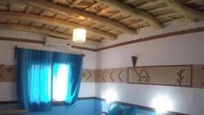 Een kamer met een houten plafond, twee bedden met blauw beddengoed, een ladder en een raam met blauwe gordijnen.