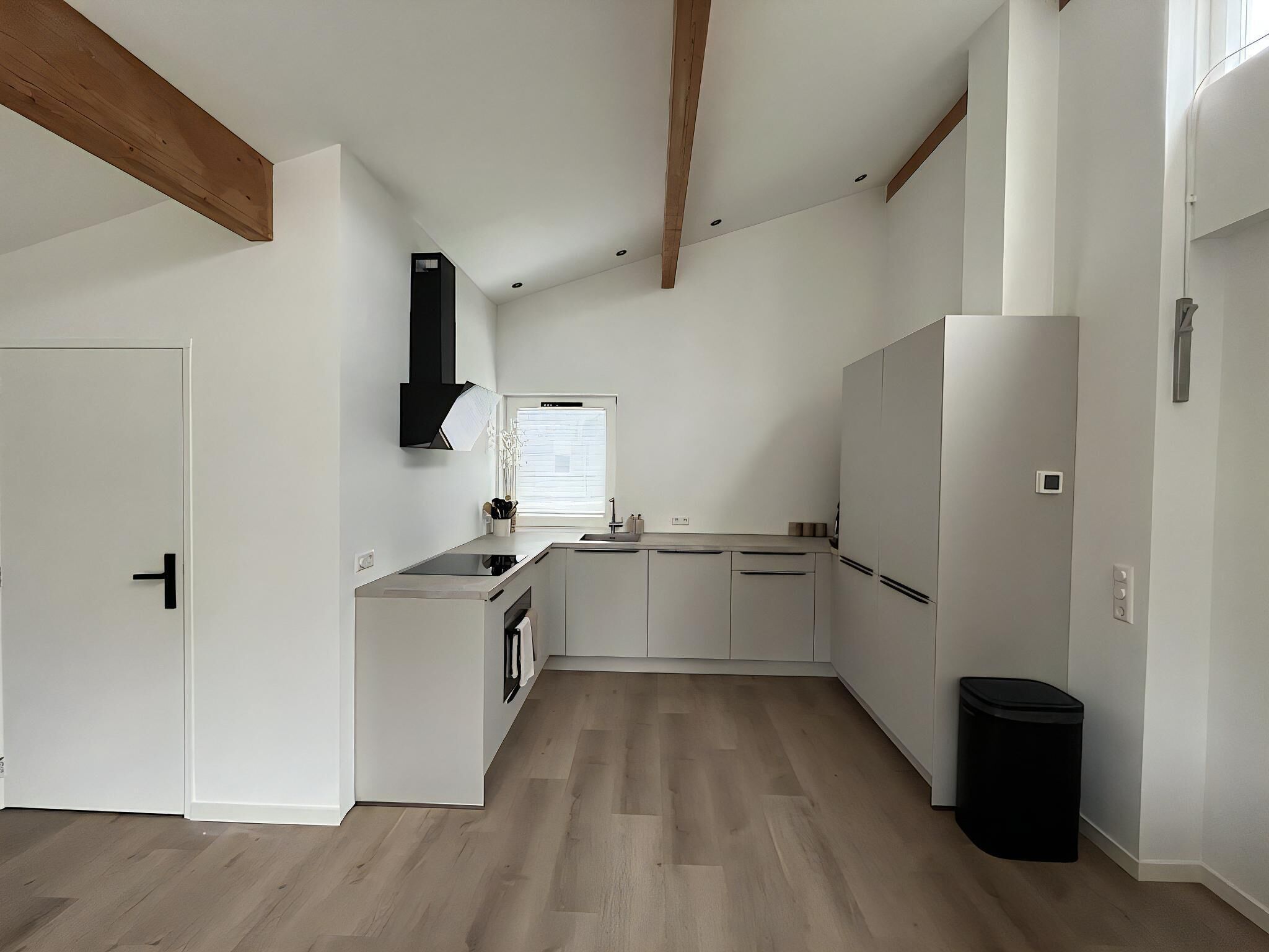 Een moderne keuken met witte kasten, een zwarte afzuigkap en een raam met jaloezieën.