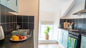 A kitchen with black tiles, a sink, a stove, and a window with a plant.