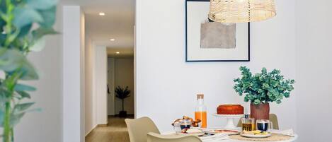 Un comedor con una mesa dispuesta para el desayuno, una lámpara colgante de mimbre y una obra de arte enmarcada en la pared.