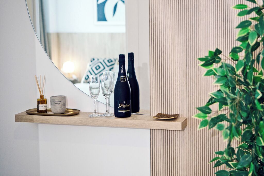 A wooden shelf with two bottles, a candle, and three glasses.