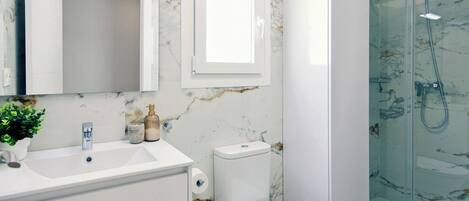 A bathroom with a marble wall, a white sink, a toilet, and a glass-enclosed shower.