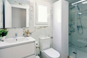 Une salle de bain avec un mur en marbre, un lavabo blanc, des toilettes et une douche à parois de verre.