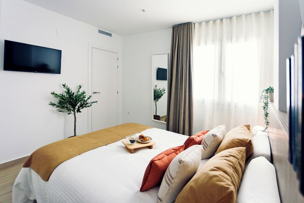 A modern hotel room with a bed, a sofa, a TV, and a window with curtains.