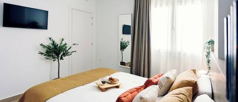 A modern hotel room with a bed, a sofa, a TV, and a window with curtains.