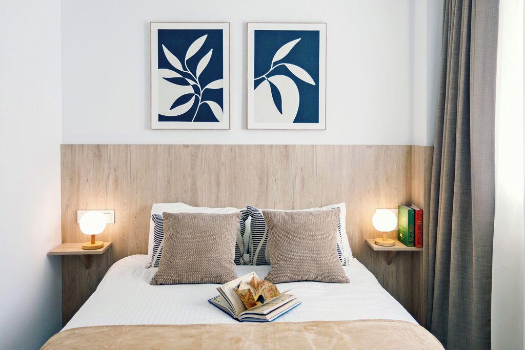 A neatly made bed with pillows, two bedside tables with lamps, and two framed wall art pieces.