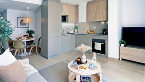 A modern kitchen with a microwave, oven, and wooden cabinets. There is a dining area with chairs and a table, and a living area with a sofa and a TV. - REM II Torrevieja (Torrevieja)
