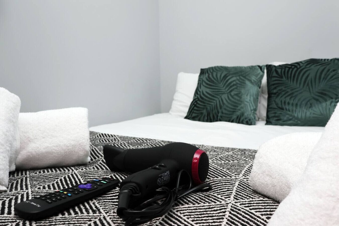A hotel room with a bed, pillows, a blanket, a remote control, and a camera.