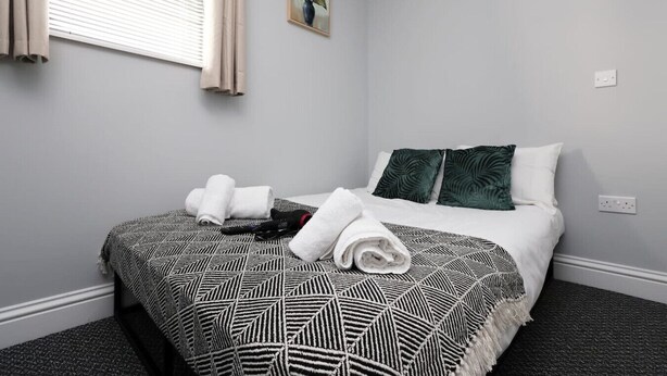 Une chambre d’hôtel avec un lit, une fenêtre avec des rideaux, une plante fixée au mur et une prise de courant.