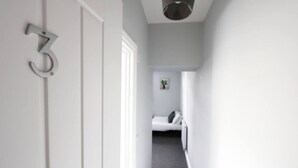 Un couloir avec une porte portant le numéro 3, qui donne sur une pièce contenant un lit et une petite plante.