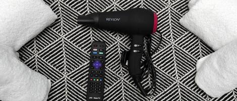 A black hair dryer and a remote control on a patterned fabric surface.