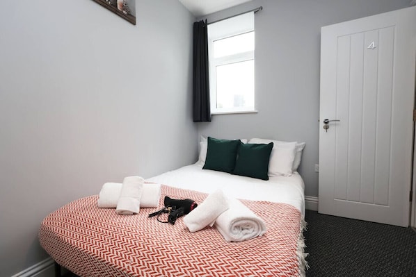 A hotel room with a bed, pillows, a window, a door, and a towel on the floor.