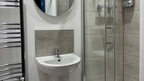 Un baño moderno con ducha envuelta en vidrio, un espejo redondo y un lavamanos blanco.