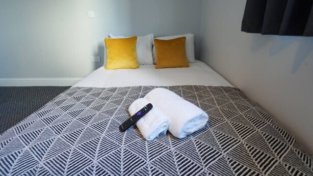 Habitación de hotel con cama, dos almohadas, un control remoto y una toalla enrollada.