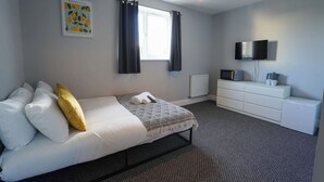 Un dormitorio con cama, cómoda, televisor y ventana con cortinas.