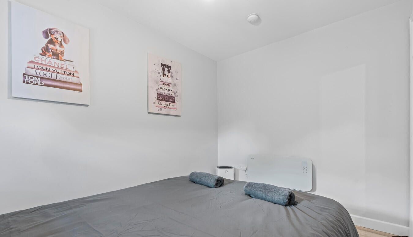 Un dormitorio con cama, almohadas, una mesita de noche y dos carteles en la pared.