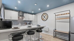 A modern kitchen with a bar area, white cabinets, a clock, and a hanging rack. - Bella`s Lodge - near Motor Point Arena (Nottingham)