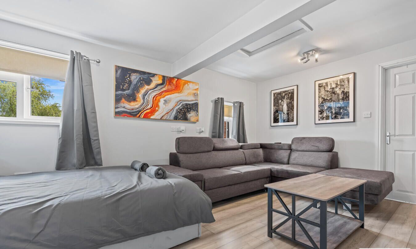 A modern bedroom with a bed, a gray sofa, a wooden coffee table, and artwork on the walls.