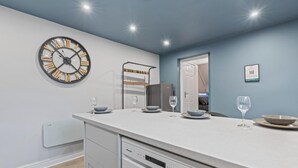A modern kitchen with a built-in clock, a dishwasher, and a dining area with a table set for two. - Bella`s Lodge - near Motor Point Arena (Nottingham)