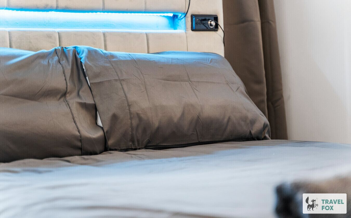Una cama con cabecera, una ventana con vistas y el logo de Travel Fox.